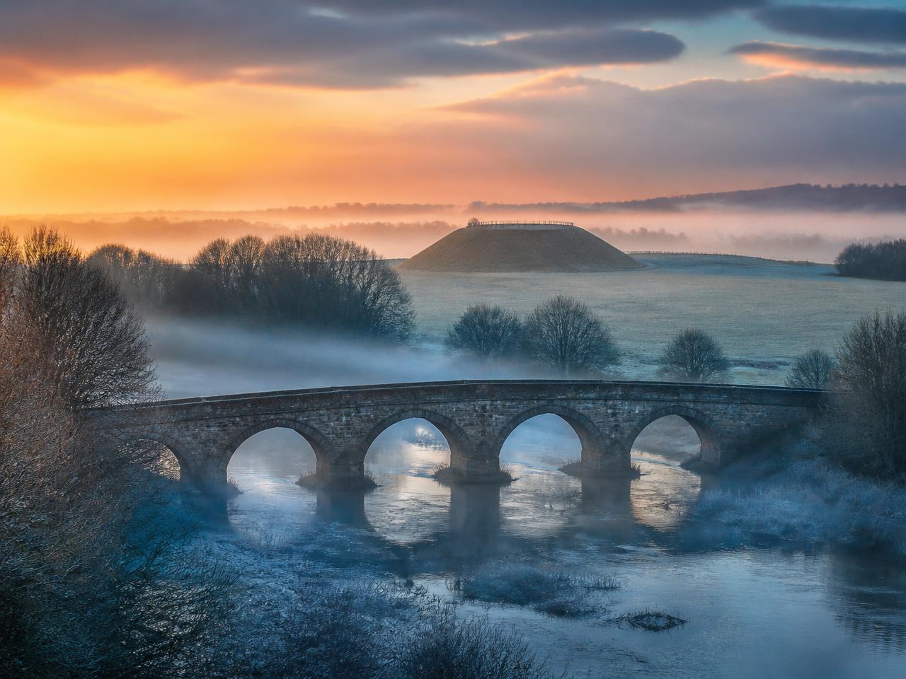 The Boyne valley at dawn: mist over the river, an old stone bridge and an ancient mound beyond