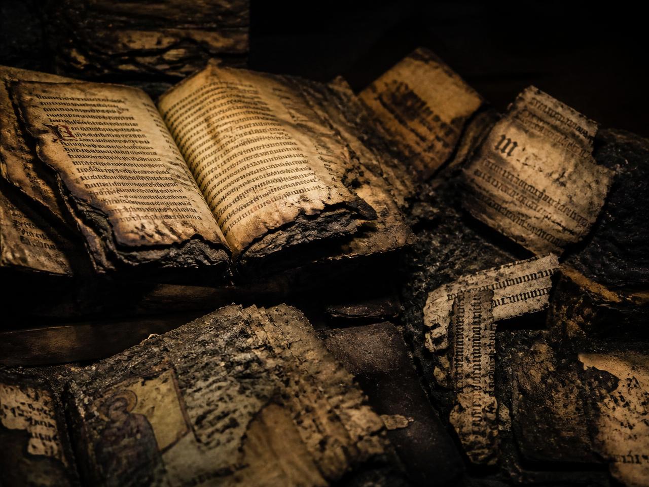 Charred medieval manuscripts and burnt parchment fragments lit in a dark archive