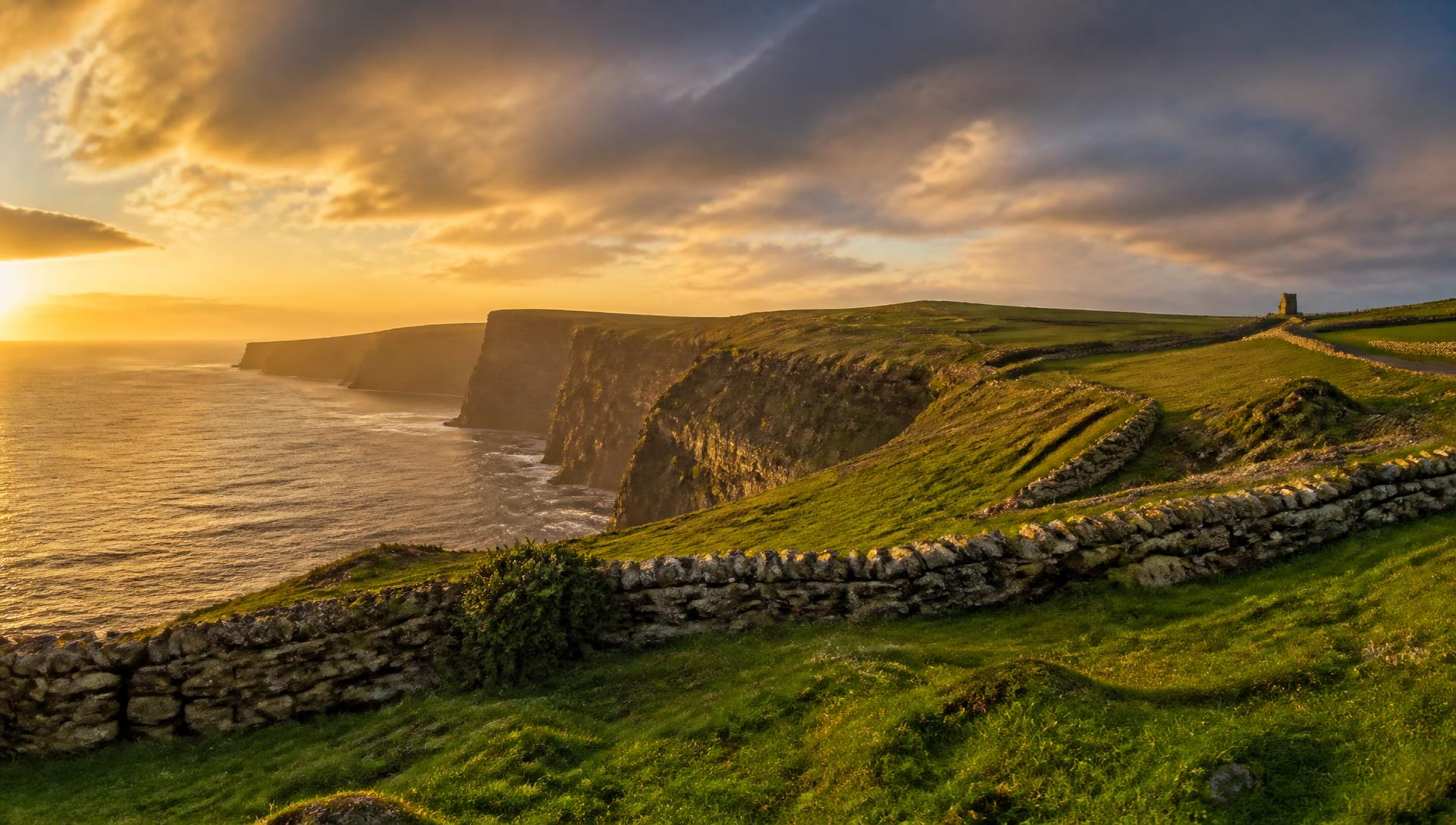 Golden-hour light over the Cliffs of Moher, with dry-stone walls crossing the green Irish headland